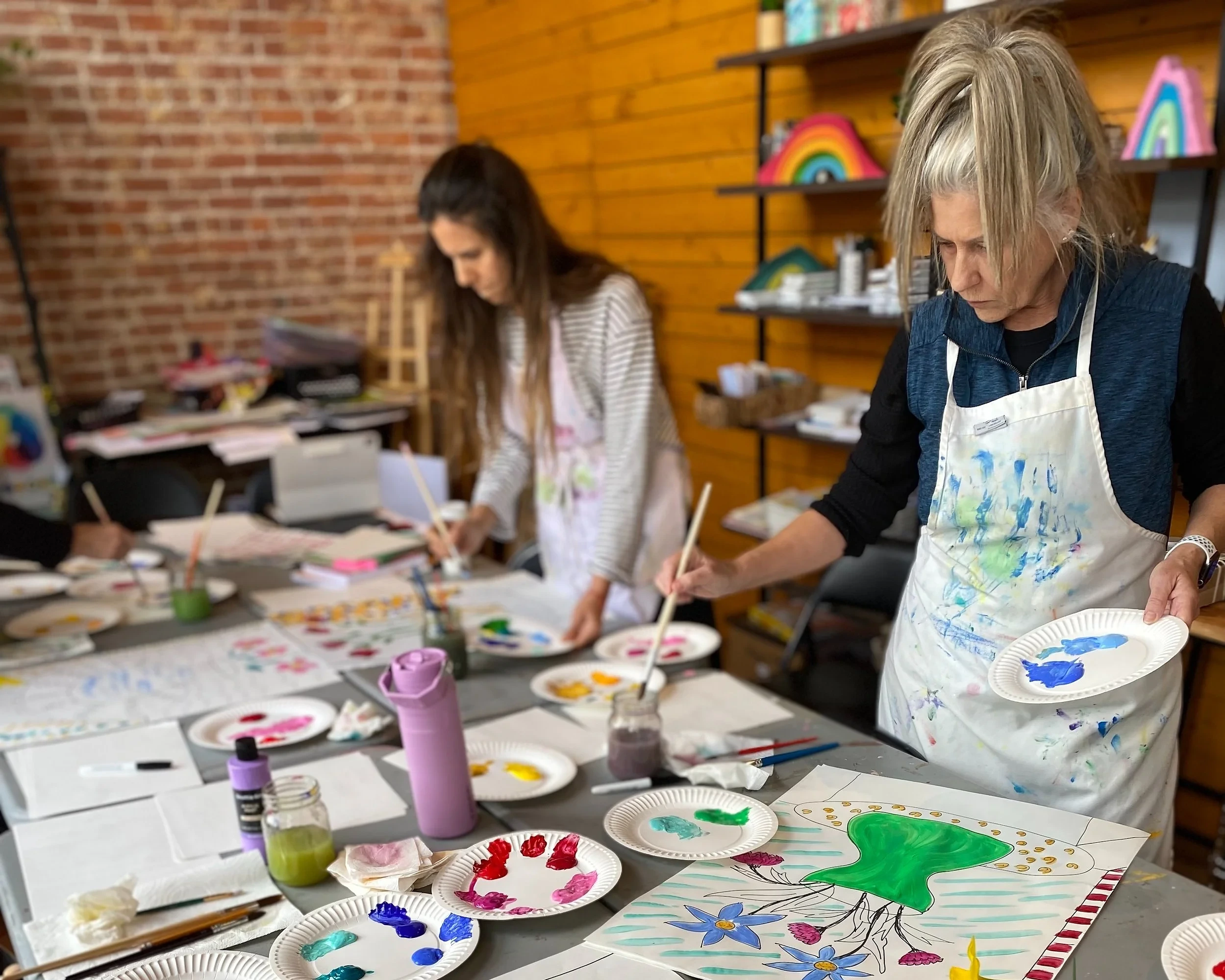Two adults painting colorful florals at a studio table during an Artaluma class